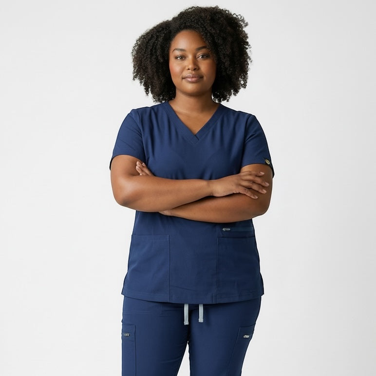 Scrubs Galore Uniforms navy blue v-neck scrub top with short sleeves and two front pockets. Model is wearing the top with arms crossed.
