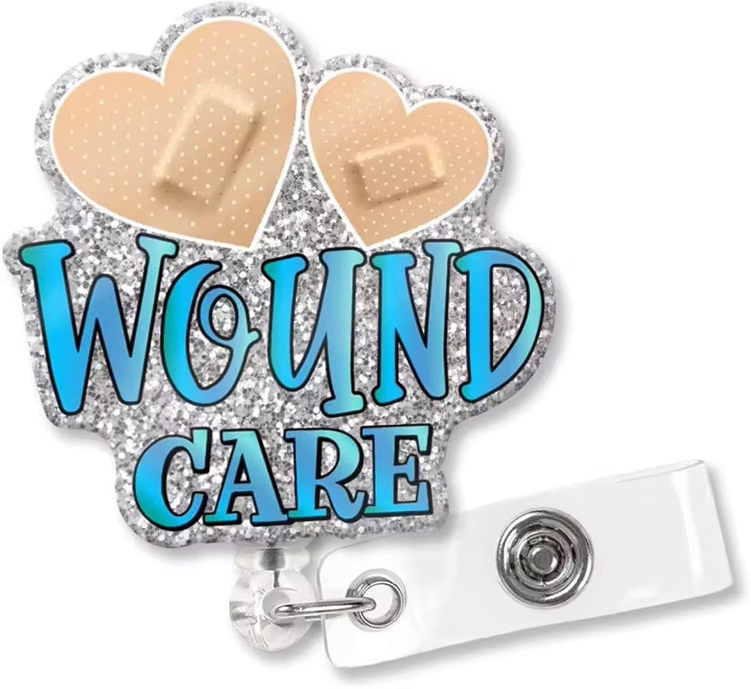 Scrubs Galore Uniforms "Wound Care" badge reel with silver glitter, two heart bandages, and blue lettering. Retractable.